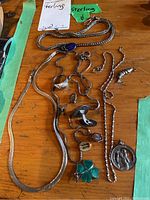 Overview of two herringbone chains, charm necklace, ring and cufflink arranged on table