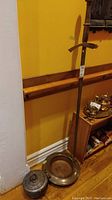 Full view showing metal sword, brass pot, and metal container with lid placed on hardwood floor against yellow wall