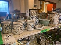 Wide view of ceramic tea set items arranged on a shelf showing cups, saucers, the bowl, and teapot with distinctive blue floral designs.
