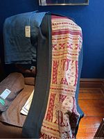 Two folded textiles on a chair; one dark reddish fabric with intricate light motifs and black border, the other solid dark blue textile.