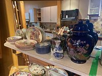 Overview of plates, vases, jars, and trinket boxes on display shelf in home kitchen setting