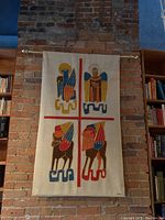 Wide view of complete wall hanging mounted on brick wall with brass rod and hooks showing full artwork.