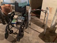 Overall view showing wheelchair, walker, pill organizer, glasses, and gauze container grouped together in a basement setting.