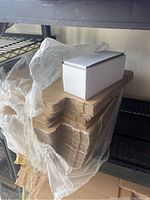 Photo showing folded flat white cardboard box forms stacked with one assembled box on top showcasing size and shape.