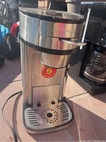 Front angled view of Hamilton Beach single cup coffee maker showing stainless steel body, drip tray, and black plastic accents.