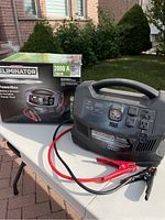 Unit and original box on table outdoors, jumper cables attached