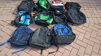 Nine backpacks in various colors and designs arranged on a paved surface.