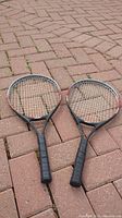 Two Cooper aluminum tennis rackets placed side by side on brick pavement.