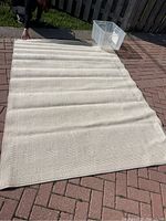 Full view showing cream wool rug laid out on a brick patio to display size and shape.