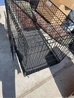 Black metal dog crate placed on concrete floor, showing the crate structure and size.