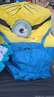 Deflated large yellow inflatable Minion costume with black stripes and a large eye visible, blue pants part shown