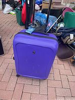 Photo of purple hard shell luggage with extended telescoping handle and wheels on pavement.