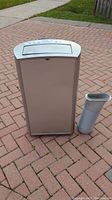 Front view of Insignia portable air conditioner next to vent hose attachment on brick surface outdoors.