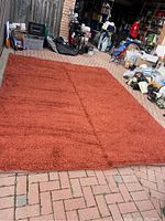 Full view of terracotta shag rug laid flat on brick floor showing texture and size