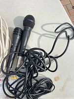 Two handheld black wired microphones with coiled cables on a white table.