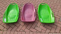 Set of three Pelican Snow Runner sleds on brick surface, two green and one purple, showing overall condition and shape.