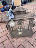 View showing the front and left side of the rectangular rod iron lantern with glass panels and floral metal decoration, including attached tag and a blue decorative flower.