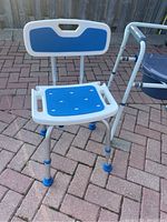 Blue and white shower chair showing front and slight angled view, highlighting the adjustable legs, padded seat and backrest with ventilation holes, and hand grips.