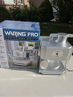 Waring Pro snow cone maker next to its original box showing the product and branding.