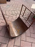 Side angled view showing the curved metal base with some rust and the upright vertical bar frame.