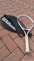 Wilson Hope tennis racket on pavement with carrying case beside it