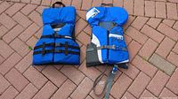 Two youth life jackets on patio bricks, showing front view with adjustable straps and handles.