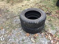 Two black Hankook tires size 195/60R15 stacked on gravel outdoors with dry leaves nearby.