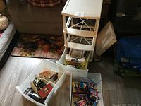 Photo showing white plastic 3-drawer organizer with drawers pulled out revealing contents including cords, small brush, and packaged items.