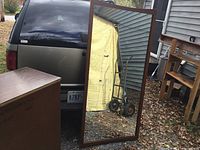 Front view of the wooden framed full-length wall mirror reflecting an outdoor scene.