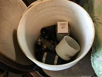 Top down view of 5 gallon pail with ABS plumbing fittings inside, showing various black fittings and a large white coupling.