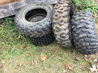 Four used ATV tires arranged side-by-side outdoors, showing tread pattern and dirt wear.