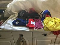 Lot of sports ball caps, gloves, and scarves arranged on a white cloth surface with a white background, showing all items in the lot.