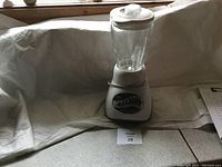 Full view of Oster blender with glass jar and white base on a fabric background.