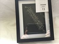 Front view of black frame containing the silver-tone bracelet with cracked glass on back