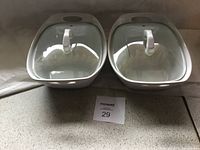 Two white covered casserole dishes with lids, each lid has a handle and steam vent.