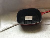 Square cast iron frying pan with ridged grill surface and red handle.
