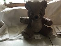Front view of a large textured brown ceramic teddy bear with coin slot and facial details, sitting on a white cloth.