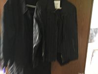 Full front view of black medium Rickis leather coat hanging on a door, showing zipper closure and smooth leather material.