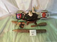 Photo showing two Coca-Cola mugs, wooden turtle keepsake box with butterfly, and three small wooden carved items arranged on a light green surface.