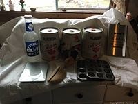 Photo showing three empty metal mini kegs branded Bubba Canadian, Maple Leafs glass piggy bank, muffin tins, wooden honey dipper and holder, small white dish, and engraved metal wallet.