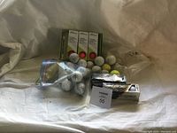 Golf balls including new boxed Titleist balls, several loose balls in white and yellow colors, and used balls in a zip-lock bag.