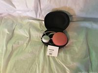 Google Nest Mini in coral color with black carrying case and white power cable shown inside case on light fabric background.