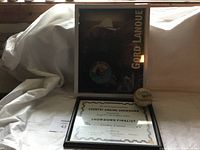 Framed display showing signed baseball, vinyl record, certificate and photo of Gordon Lanoue in a cowboy hat.