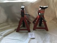 Pair of red metal jack stands with 2 ton capacity labels, adjustable height ratchet mechanism visible, in new condition, photographed from front angle.