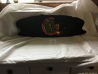 Top side of skateboard deck showing black surface with Santa Cruz logo in colorful letters.