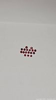 Photo showing multiple small round deep red natural heated rubies arranged on a grey background with visible luster and color variation in size from 2mm to 2.5mm