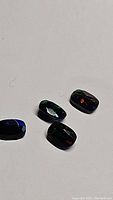 Four faceted black Ethiopian opal gemstones showing red, green, and orange play of color against white background.