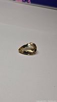 Clear photo of a pear shaped golden citrine gemstone placed on a white surface showing its cut and clarity.