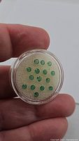 Top view of calibrated round Zambian emeralds in a small clear round display case, held by hand, showing vibrant green color and clarity.