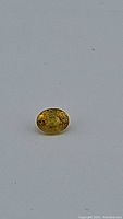 Close-up image of the oval faceted yellow sapphire gemstone with visible inclusions on a plain surface.